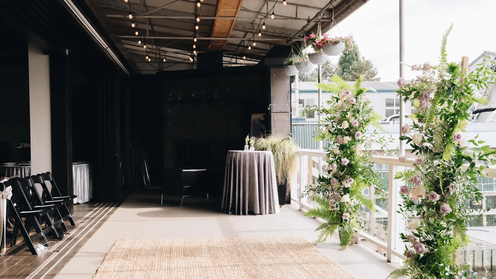 The covered patio set for a ceremony, with a floral arch framing the railing and a woven aisle runner leading to it.