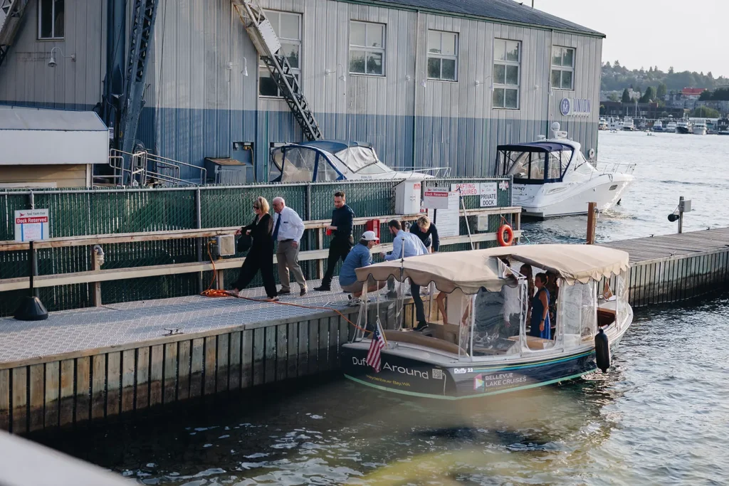 Guests stepping off a covered water shuttle onto the dock, with private boats and Lake Union behind them.