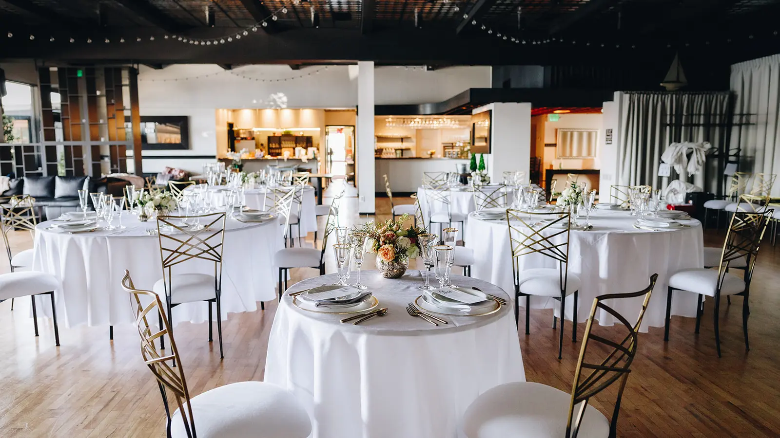 The main room set at rounds for a reception, with the bar visible through the pass-through and a lounge area along the far wall.