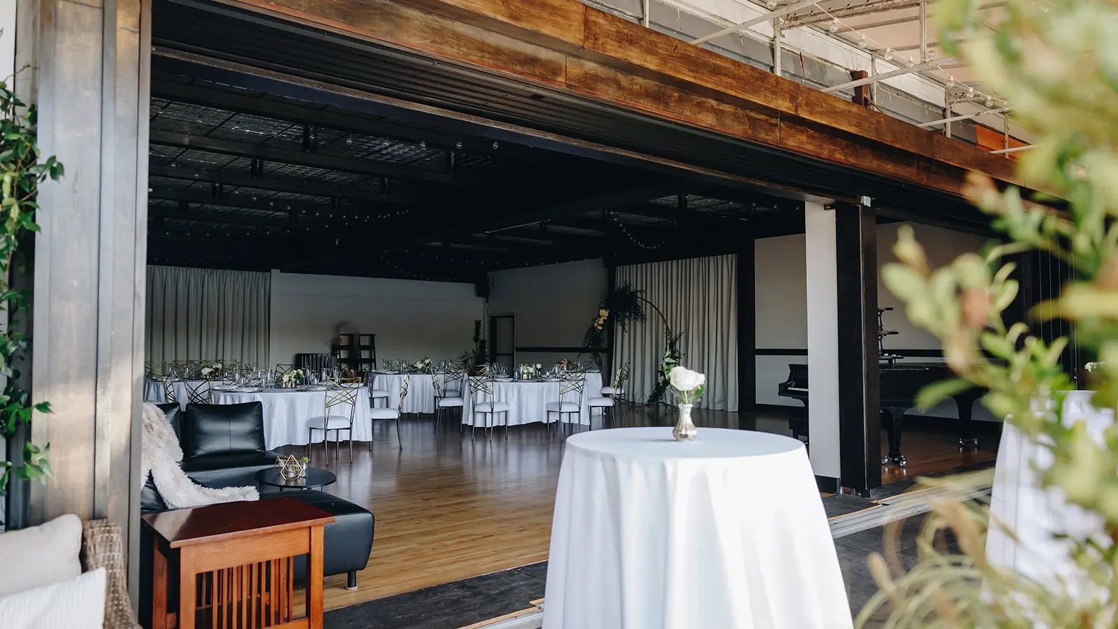 Round tables in white linen and a wood dance floor in the main room at our Lake Union venue, seen through the open wall from the lounge seating outside it.